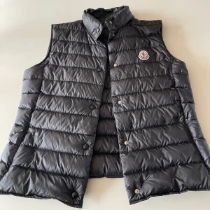 Moncler Väst - En väl använd Moncler Väst som är ca 6 år gammal. Den är fortfarande i väldigt bra skick men den har tyvärr blivit lite för liten för mig. Den är i en storlek 2, som jag skulle säga motsvarar XS-S. Den är 100% äkta och det tillkommer även lite tillbehör jag fick när jag köpte den i Stockholm. Den största defekten är att det står mitt efternamn inuti västen (se bild 3). Nypris för denna är ca 5000-6000kr.