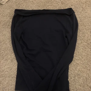Mörkblå med en halv offshoulder topp Gina Tricot - Snygg mörkblå offshoulder topp från Gina Tricot i storlek XS. Toppen har långa ärmar och är tillverkad i mjuk bomull. Enkel och stilren design som ger en cool vibe, perfekt att matcha med jeans eller kjol. Passformen är slim och tyget är stretchigt. Tröjan är inte helt offshoulder utan bara lite