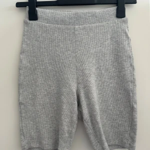 Grå ribbade cykelshorts - Säljer ett par grå ribbade cykelshorts med hög midja. De är stretchiga och sitter tajt, perfekta för en chill look eller till träning. Materialet är mjukt och bekvämt, och shortsen har en enkel, stilren design utan synliga detaljer eller fickor.