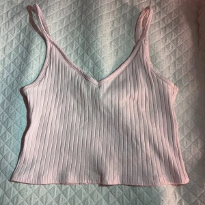Ljusrosa ribbad linnetopp - Säljer en ljusrosa ribbad linnetopp med smala axelband och v-ringning. Toppen är croppad och har en tight passform som framhäver figuren. Perfekt för varma dagar eller att styla lager på lager. Materialet är mjukt och stretchigt för extra komfort! ❤️