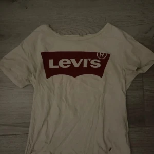 Vit Levi's t-shirt med röd logga - Vit t-shirt från Levi's med klassisk röd logga tryckt på bröstet. Modellen har rund hals och korta ärmar. Tillverkad i mjuk bomull och har en liten röd Levi's-tag på sidan. Perfekt för dig som gillar ikoniska streetwear-plagg.