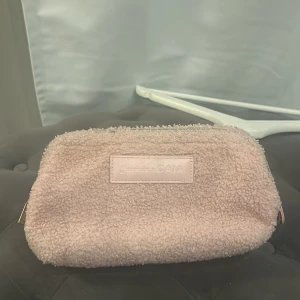 Rosa necessär Jasmine x CAIA - Supergullig rosa necessär från Jasmine x CAIA med mjuk teddytextur på utsidan och flera fack inuti. Perfekt att ha smink eller småprylar i. Stängs med dragkedja och har en stilren, enkel design.