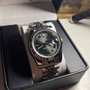 Seiko ”Wimbledon” Mod - Helt nybyggd Seiko ”Wimbledon” Datejust Mod  Specifikationer: Storlek: 39mm Urverk: Nh35 (Automatiskt) Material: 904L Rostfritt Stål Glas: Sapphire Glas Boett: Räfflad Bezel Tavla: Wimbledon  Armband: Viklås och Justerbart  Krona: Screw Down Vattentålighet: 30 Meter Klocklåda ingår