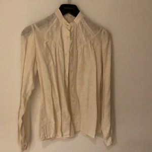 Offwhite blus med spetsdetaljer, sekelskiftestil  - Säljer en beige skjorta från Bianca med lång ärm och snygga spetsdetaljer över axlar och rygg. Den har knappar framtill och en hög krage som ger en clean look. Perfekt för dig som gillar stilrena plagg med en twist. Storlek 36. 100% bomull.