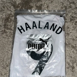 Manchester City Haaland tröja Puma M - Säljer en officiell Manchester City fotbollströja från Puma med Haaland och nummer 9 på ryggen. Tröjan är vit med grått mönster, har en diagonal svart och röd rand på framsidan samt broderat klubbmärke. Tillverkad i återvunnet material och med DryCell-teknologi.