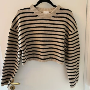 Randig beige och svart stickad tröja H&M - Snygg croppad stickad tröja från H&M i beige med svarta ränder. Tröjan har rund hals, ribbade muddar och lång ärm. Perfekt för hösten🍁🍁