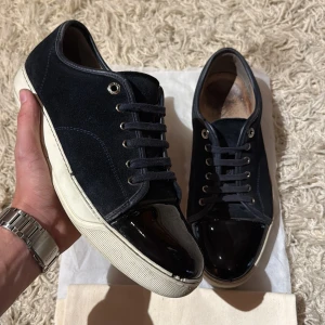 Lanvin - Säljer nu dessa sjukt snygga sneakers från Lanvin med ovandel i mocka och en glansig lackad tå. Perfekta för dig som gillar en stilren men ändå unik look. Size Uk9 vilket motsvarar 43-44! Skick: 7/10! Hör av dig vid minsta lilla fundering🤩dustbag medföljer👍