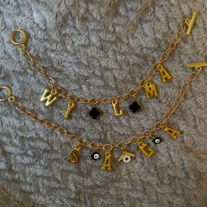 Guldiga armband med bokstavsberlocker - Två chunky guldarmband med kedja och hängande bokstäver som bildar namn. Armbanden har svarta och vita berlocker, bland annat ögon och fyrklöver. Perfekt accessoar för dig som vill sticka ut med personliga detaljer. Du får själv välja det du vill ska stå på armbandet 🤍