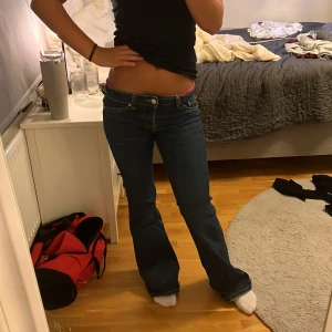 Blå bootcut jeans från H&M Divided - Säljer ett par blå bootcut jeans från H&M Divided i storlek 34. Jeansen har låg midja, klassiska fickor och snyggt utsvängda ben. Tillverkade i jeansmaterial med kontrastsömmar. Perfekta för dig som gillar retrovibbar och en avslappnad look.