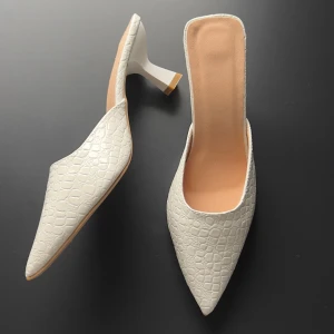 Vita pumps med spetsig tå och klack - Säljer ett par vita pumps med spetsig tå och låg klack. Skorna har en snygg krokopräglad yta i syntetmaterial och öppen häl. Perfekta för dig som vill sticka ut med en stilren och trendig look.