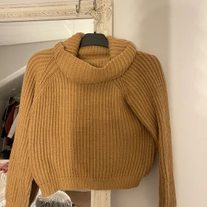 Stickad polotröja i camel - Mysig stickad polotröja i camelbrun färg med  ribbstickning. Tröjan har en hög, bred polokrage och långa ärmar. 