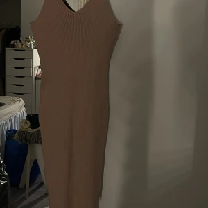 Stickad beige midiklänning - Stickad beige långklänning med v-ringning och smala axelband. Klänningen är figurnära och har en , minimalistisk look. Materialet är stretchigt och bekvämt.
