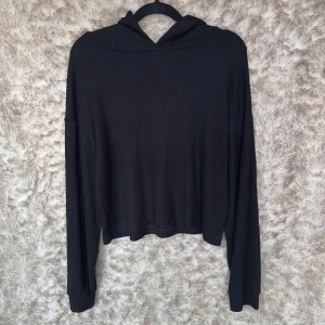 Svart ribbad hoodie från Gina Tricot - Svart ribbad hoodie från Gina Tricot i storlek S. Tröjan har lång ärm, huva och är tillverkad i ett mjukt, stretchigt material. 