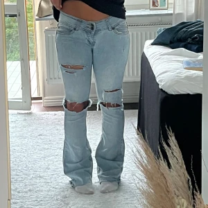 Lågmidjade ljusblå bootcut jeans  - Säljer ett par ljusblå jeans med bootcut-modell och slitningar över knäna. Jeansen är väldigt låg midjade och as snygga. 