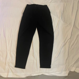Svarta mjukisbyxor med vit rand - Svarta mjukisbyxor med en vit rand längs sidorna. Byxorna har en avslappnad passform och resår i midjan. Perfekta för chill dagar eller när du vill vara bekväm men ändå se snygg ut.