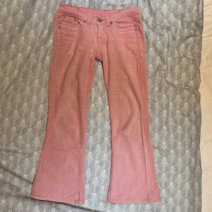 Rosa bootcut manchesterbyxor - Säljer ett par snygga rosa manchesterbyxor från Up 2 Jeans med bootcut-modell och väldigt låg midja. Byxorna har klassiska fem fickor, silverfärgade nitar och tydlig manchesterstruktur. Perfekta för dig som vill sticka ut med färg och retrovibe. De är verkligen så snygga men tyvärr för korta för mig som är 166cm lång. Midjemått rakt över: 38cm, innerbenslängd: 70cm