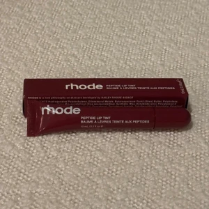 Rhode Peptide Lip Tint ”raspberry jelly” - Rhode Peptide Lip Tint i en bärig, mörkröd nyans. Kommer i en smidig tub med skruvkork och rymmer 10 ml. Ger läpparna en snygg tint och innehåller peptider för extra vård. Perfekt för dig som vill ha både färg och återfuktning i ett.