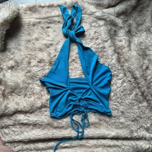 Turkos halterneck topp med knyt - Säljer en turkos halterneck topp med breda knytband i nacken och snygg snörningsdetalj framtill. 