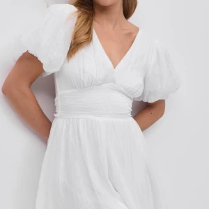 Vit kortklänning med puffärm - Superfin vit klänning med v-ringning och bred midjedetalj. Klänningen har puffiga korta ärmar och är tillverkad i ett lätt, strukturerat tyg som ger en luftig känsla. Perfekt till studenten. Aldrig använd, prislapp sitter kvar!!