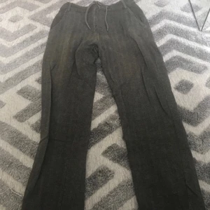 Mörkgrå byxor med snörning från Kappahl - Mörkgrå byxor från Kappahl i storlek 158. Byxorna har snörning i midjan, elastisk linning och raka ben. De är tillverkade i ett mjukt material som känns skönt mot huden och har fickor både fram och bak. Perfekta för en chill och avslappnad stil.