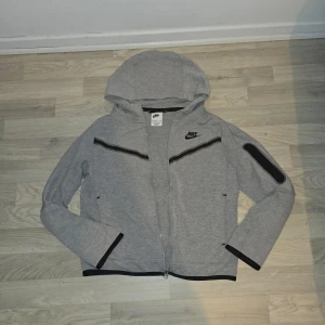 Grå Nike tech kofta - Säljer en grå Nike tech. Använd och färgen är skrapad ifrån dragkedjan. Perfekt för en sportig och chill stil. Priset kan bli sänkt.