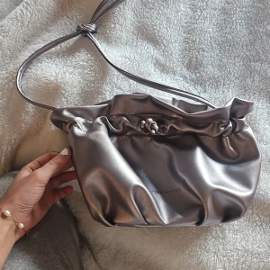 Silver axelväska från Carin Wester - Snygg axelväska i metallic silver från Carin Wester. Man kan såklart göra banden längre. Fint skick😍