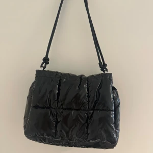 Svart quiltad axelväska från H&M - Quiltad svart axelväska från H&M med glansig finish. Väskan har ett stort huvudfack med dragkedja. Perfekt storlek för att få plats med allt du behöver. ❣️