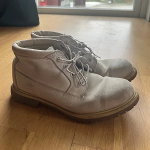 Timberland boots  - Säljer ett par klassiska Timberland boots i beige nubuck med grov sula och snörning. Skorna har rund tå och robust design, perfekta för dig som gillar street och outdoor-vibe. Timberland-loggan syns på sidan. Nubuck cleaner medföljer vid extra 100 lapp. Mer information, photos och prisdiskutering i dm.  