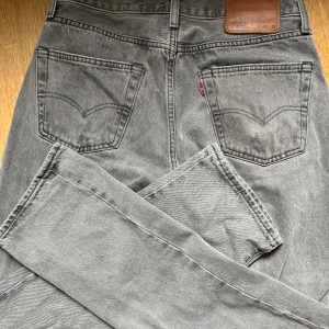 Grå Levi's 501 jeans straight fit - Säljer ett par grå Levi's 501 jeans i straight fit med klassisk femficksdesign och knappgylf. Jeansen är tillverkade i denim och har den ikoniska läderpatchen bak i midjan. Perfekta för dig som gillar en tidlös och clean look.