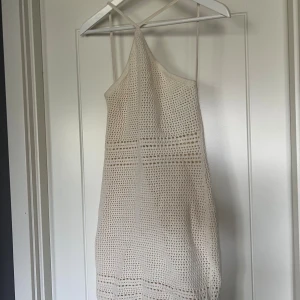 Beige virkad kortklänning med öppen rygg - Beige virkad kortklänning med halterneck och öppen rygg. Klänningen är genomskinlig. Perfekt för varma dagar eller över bikinin.