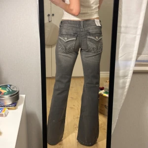 Grå bootcut jeans med broderade fickor - Gråa bootcut lågmidjade jeans från Gina Tricot med snygga broderade detaljer på bakfickorna. Helt nya med lapparna kvar, bara testare, så sköna med stretch, storlek 158 men passar en XS/34 och längre än de då jag är ca 160 och de är lite långa på mig 