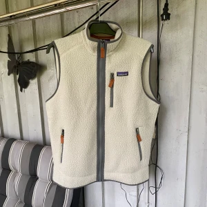 Patagonia väst - Snygg beige  fleeceväst från Patagonia med grå detaljer. Västen har hög krage och tre praktiska fickor med dragkedja. Perfekt för lager-på-lager. Aldrig använd!