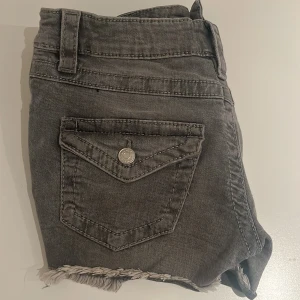 Grå jeansshorts med fransig kant - Grå lågmidjade jeans shorts från Gina, med fickor bak.