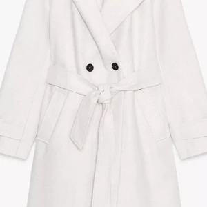 Vit kappa med bälte och knappar har inte använten funkar för xs och s fräsch färg och funkar med allt säljer den för 450 men kan sälja den fel mindre  - Stilren vit kappa med bred krage, knytskärp i midjan och dubbla svarta knappar framtill. Jackan har långa ärmar och två fickor på sidorna. Perfekt för dig som vill ha en clean och klassisk look.