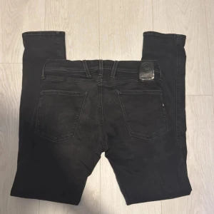  Replay Anbass Hyperflex  - Säljer ett par svarta Replay Hyperflex jeans med klassisk femficksdesign och snygga detaljer. Jeansen har en slim passform och är tillverkade i stretchigt jeansmaterial för extra komfort. Perfekta för dig som gillar stilrena och bekväma byxor. Storlek 30/32