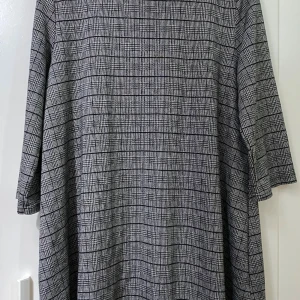 Rutig grå klänning från JYOTHI XL - Säljer en grå och svart rutig klänning från JYOTHI i storlek XL. Klänningen har en rak och loose passform med trekvartsärm och en liten öppning bak i nacken. Perfekt för dig som gillar stilrena och klassiska mönster. Grå klänning med inga fläckar på eller skada som binder på bilden! Har använt få gånger. Längden till klänningen är 81 cm och bredden (från ena axeln till det andra) är 40 cm. Meddela mig gärna för mer info! 💕