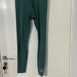 Gröna träningsleggings Quickdry M - Mörkgröna träningsleggings från lager 157 med Quickdry-teknologi. Tight passform och hög midja, perfekta för gymmet eller löpning. Snygg minimalistisk design med liten logga vid benet. Materialet är syntet och torkar snabbt.