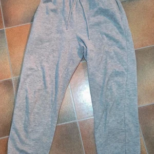 Pieces Grå Mjukisbyxor (Joggers) - Hög Midja, Strl XS (Perfekt för mys) - Säljer ett par bekväma och varma sweatpants (mjukisbyxor/joggers) från märket Pieces. Byxorna är i en klassisk mellangråmelerad färg och har borstad insida, vilket gör dem extra mjuka och mysiga.  De har en bekväm resårmidja med dragsko och muddar vid anklarna. Perfekta som ett avslappnat vardagsplagg, hemmamys eller för att ta med till gymmet.  Märke: Pieces  Storlek: XS  Färg: Gråmelerad  Material: 50% Bomull, 50% Polyester (enligt etikett).