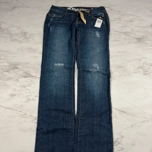 Blå jeans från Zoo York bootcut - Snygga blå jeans från Zoo York med bootcut passform och slitna detaljer framtill och baktill. Klassisk femficksmodell med normal midja och coola kontrastsömmar. Perfekta för dig som gillar streetstyle och avslappnad look.