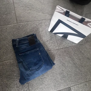 Replay Anbass Hyperflex jeans blå - Säljer ett par Replay Anbass Hyperflex jeans i klassisk blå tvätt. Jeansen har raka ben, fem fickor och snygga slitningar framtill. Materialet är stretchigt för extra komfort och passformen är slim. Perfekta för dig som gillar stilrena och bekväma jeans. Strl 30/34