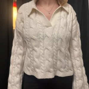 Vit kabelstickad kofta med krage - Säljer en vit kabelstickad kofta med bred krage och v-ringad hals. Tröjan har långärmade, lite loose ärmar och ribbade muddar vid ärmslut och nederkant. Perfekt för dig som gillar mysiga och stilrena plagg med chunky känsla.