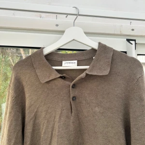 Brun pikétröja från Lindbergh - Säljer en brun långärmad pikétröja från Lindbergh med klassisk krage och tre knappar framtill. Tröjan är i mjukt material och har diskret broderad logga på bröstet. Perfekt för en clean och stilren look.