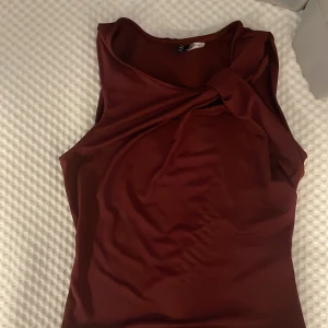 Vinröd omlott linnetopp från H&M Divided - OANVÄND Snygg vinröd linnetopp från H&M Divided i storlek S. Toppen har ett omlott-detalj vid axeln och är ärmlös med rund halsringning. Materialet är mjukt och har en lätt glansig finish som känns skönt mot huden. Perfekt för dig som gillar stilrena och trendiga plagg. Köpt för 400 säljs för 200