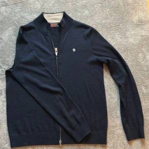 Marinblå kofta från Morris - Snygg marinblå kofta från Morris med dragkedja och diskret logga på bröstet. Tillverkad i mjuk ull och har ribbade muddar samt hög krage. Perfekt för lager-på-lager och stilren look.