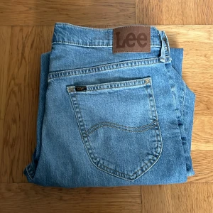 Lee Daren Zip Fly ljusblå jeans - Säljer ett par klassiska ljusblå Lee Daren Zip Fly jeans med raka ben och normal passform. Jeansen har fem fickor, dragkedjegylf och Lee-logga på bakfickan samt läderpatch i midjan. Perfekta för dig som gillar en tidlös denimlook.