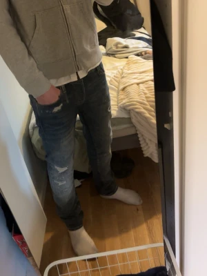 Jack and Jones jeans - Snygga blå jeans från Jack & Jones med slitna detaljer och en modern look. De har en knappgylf och klassisk femficksdesign. Perfekta för en avslappnad stil. Storlek W30 L34