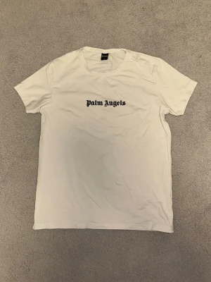 Vit Palm Angels t-shirt i bomull - Säljer en stilren T-shirt från Palm Angels i vitt. T-shirten har en cool design både fram och bak, perfekt för en trendig look. Jag är aktiv 24/7 och svarar snabbt på frågor, så tveka inte att höra av dig! Jag erbjuder snabb frakt, med möjlighet till avsändning samma dag eller nästa dag. Köp nu för att få ett snyggt tillskott till din garderob!📦🚚🚛
