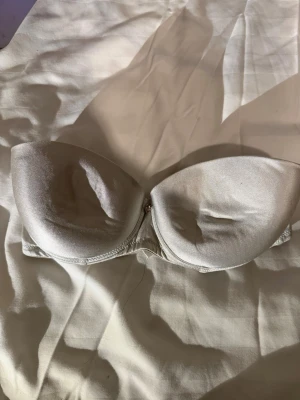 Silvrig bh smyckesdetalj💿💫 - Säljer en snygg strapless bh i silvrigt satinliknande material.  Bh-n har en glittrande smyckesdetalj mellan kuporna och slät baksida med hakknäppning. I storlek 75B. Perfekt för dig som vill ha en clean look med lite extra bling.🪩💫✨