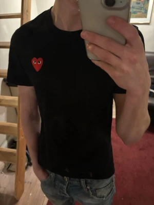 Svart t-shirt Comme des Garçons Play - Svart t-shirt från Comme des Garçons Play med klassisk röd hjärtlogga och knappt använd. Modellen är kortärmad och har en rund halsringning. Materialet är mjuk bomull som känns skön mot huden. Perfekt för dig som gillar stilrena och ikoniska plagg.