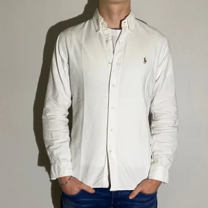 Vit skjorta från Polo Ralph Lauren - Säljer en stilren vit skjorta från Polo Ralph Lauren i storlek M. Skjortan har en slim fit passform och är långärmad med klassiska knappar. Perfekt för både vardag och festliga tillfällen. Den ikoniska loggan är broderad på bröstet. Skjortan är i mycket bra skick och gjord av bomull.